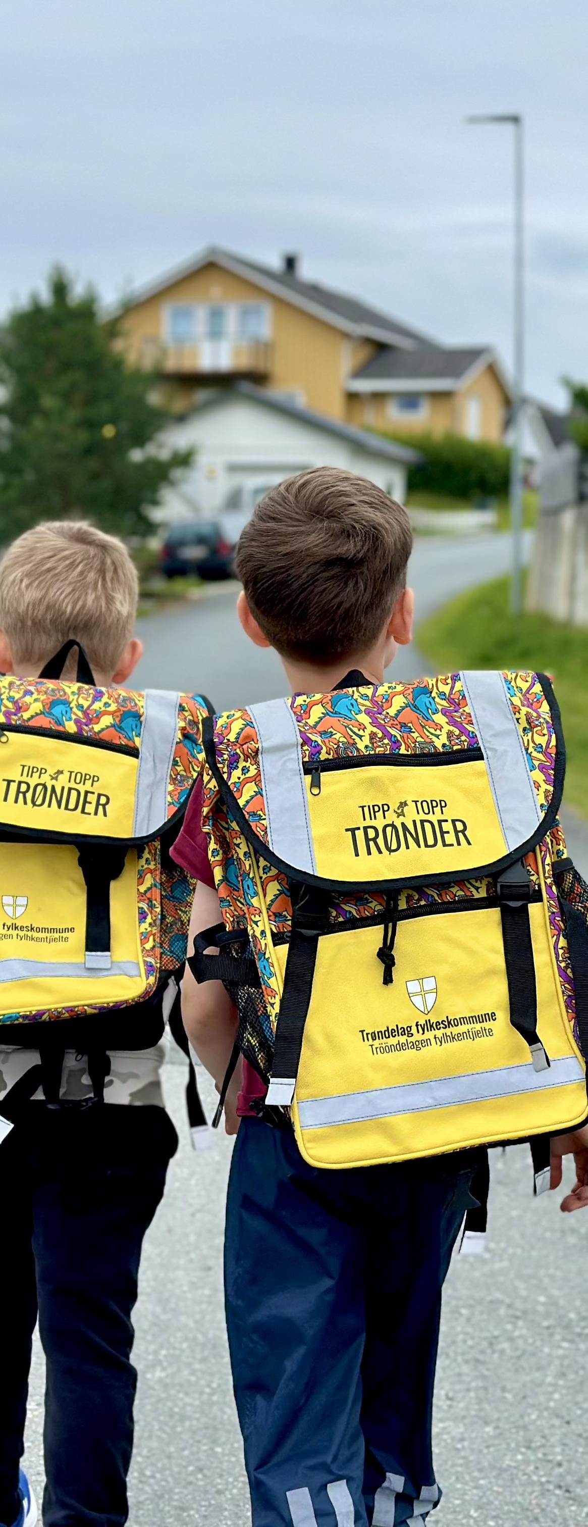 To skolebarn som går sammen bortover en gate med lik sekk på ryggen. 