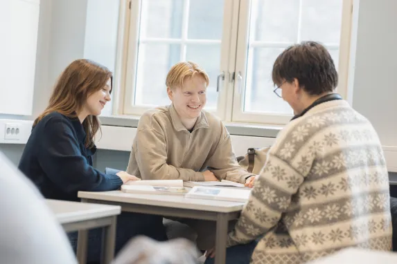 Tre smilende elever i et klasserom.